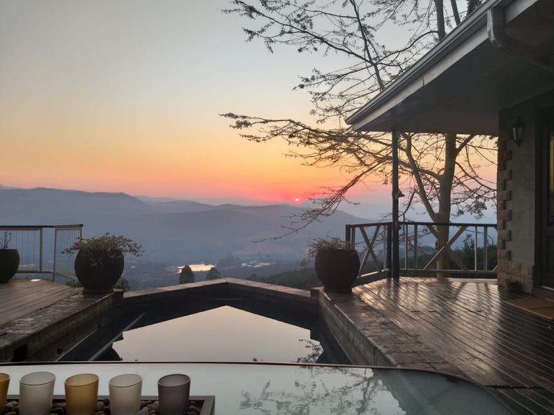 A scenic outdoor pool area featuring timber decking and a metal balustrade, offering expansive mountain views at sunset.