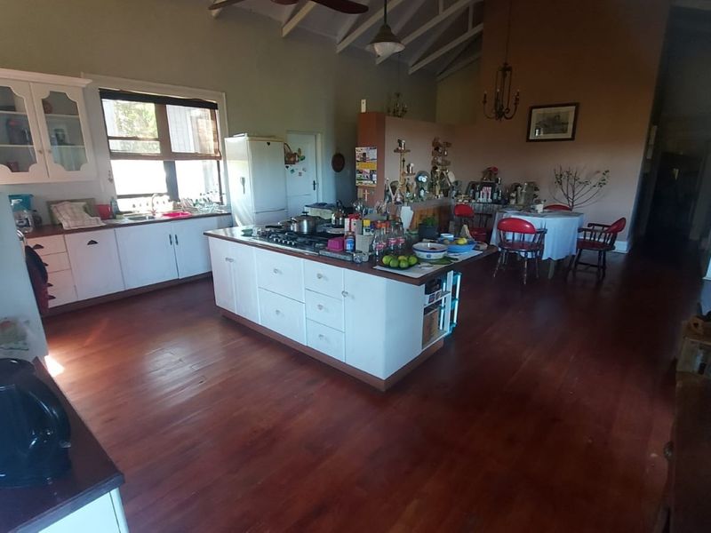 Spacious open-plan kitchen and dining area featuring hardwood flooring, a central island with a cooktop, and vaulted ceilings with exposed beams.