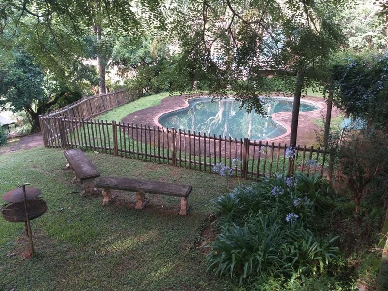 A private backyard featuring a swimming pool with brick coping, enclosed by a wooden fence and surrounded by established garden landscaping.