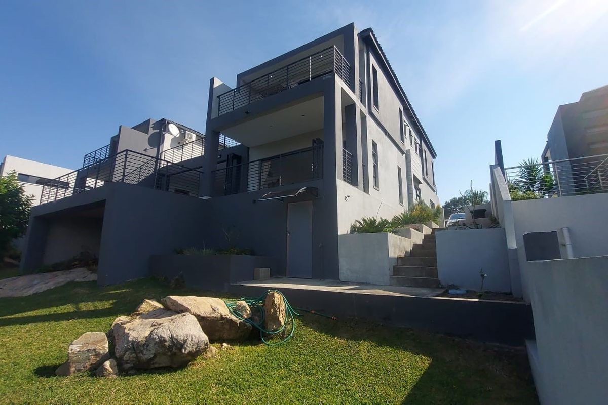 Rear view of a modern multi-level house featuring tiered balconies with metal railings, concrete stairs, and landscaped garden areas.