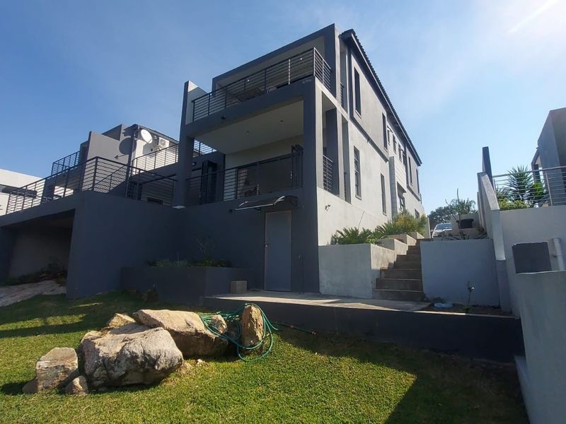 Rear view of a modern multi-level house featuring tiered balconies with metal railings, concrete stairs, and landscaped garden areas.