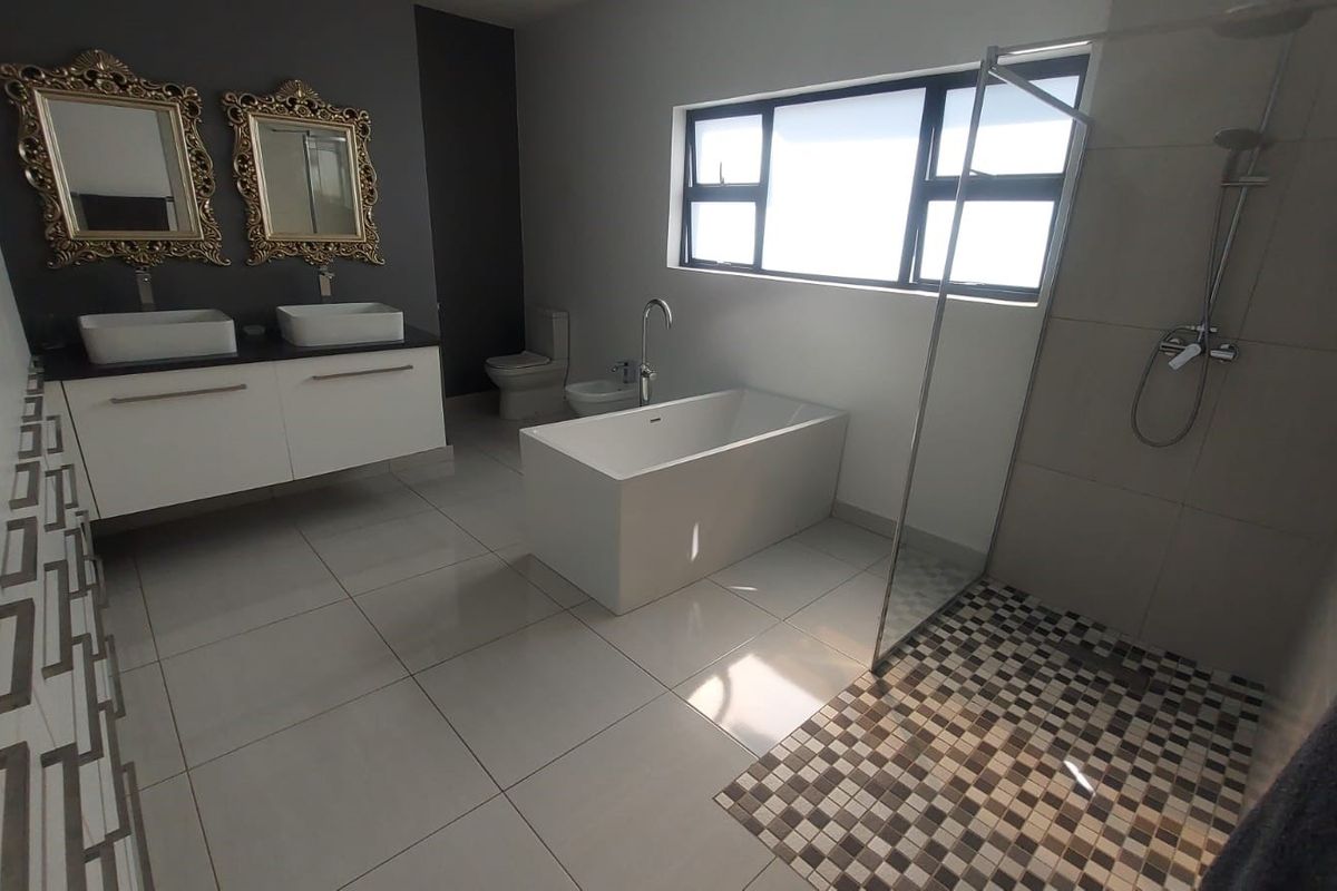 Modern bathroom featuring a double vanity with vessel sinks, a freestanding bathtub, a walk-in shower with mosaic tiling, and a separate bidet and toilet.