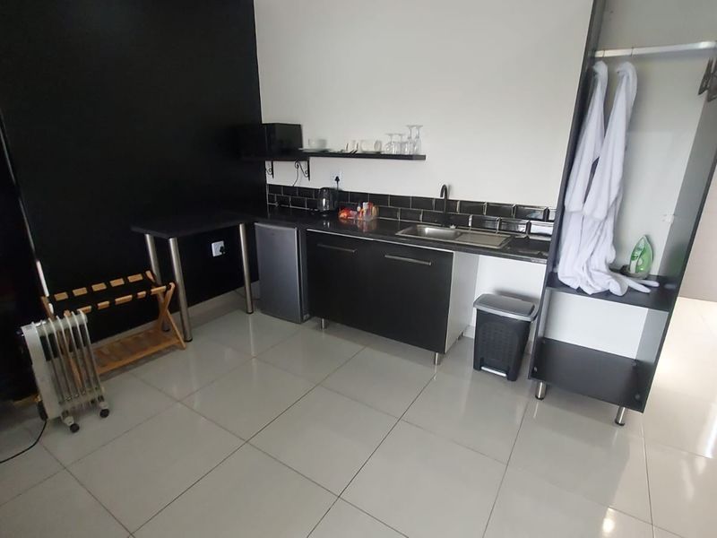 A compact kitchenette area featuring modern dark cabinetry, a sink, tiled backsplash, and an integrated wardrobe unit with tiled flooring.
