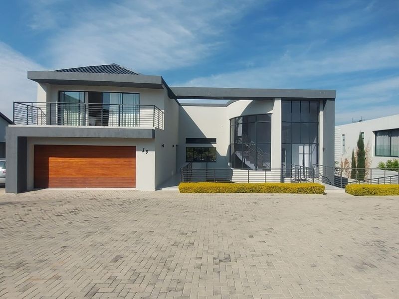 Modern double-story residential property featuring a timber garage door, upper-level balcony with metal railings, and expansive glass windows.