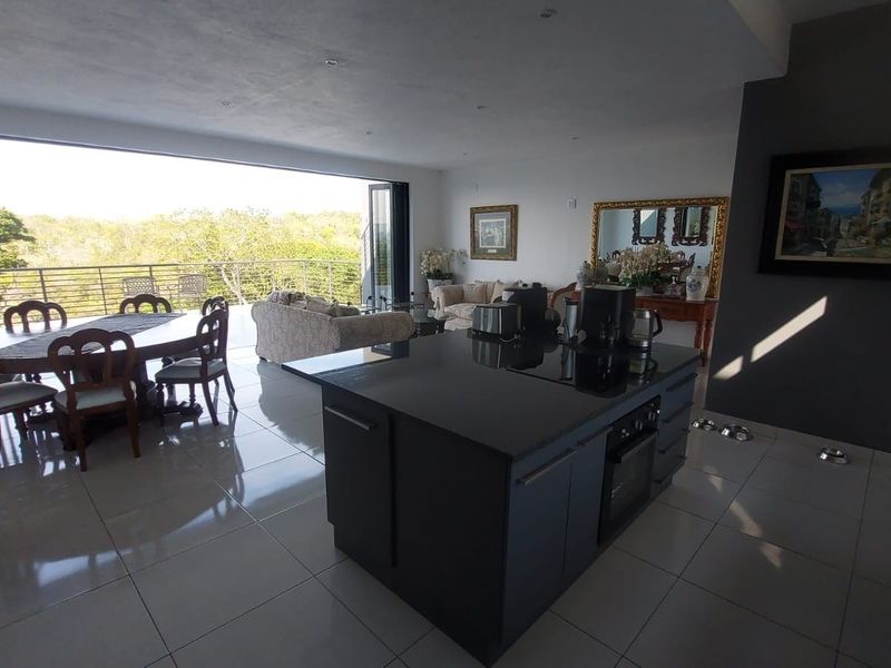 Spacious open-plan living and kitchen area featuring a central island, modern cabinetry, and large bi-fold doors opening to an outdoor balcony.