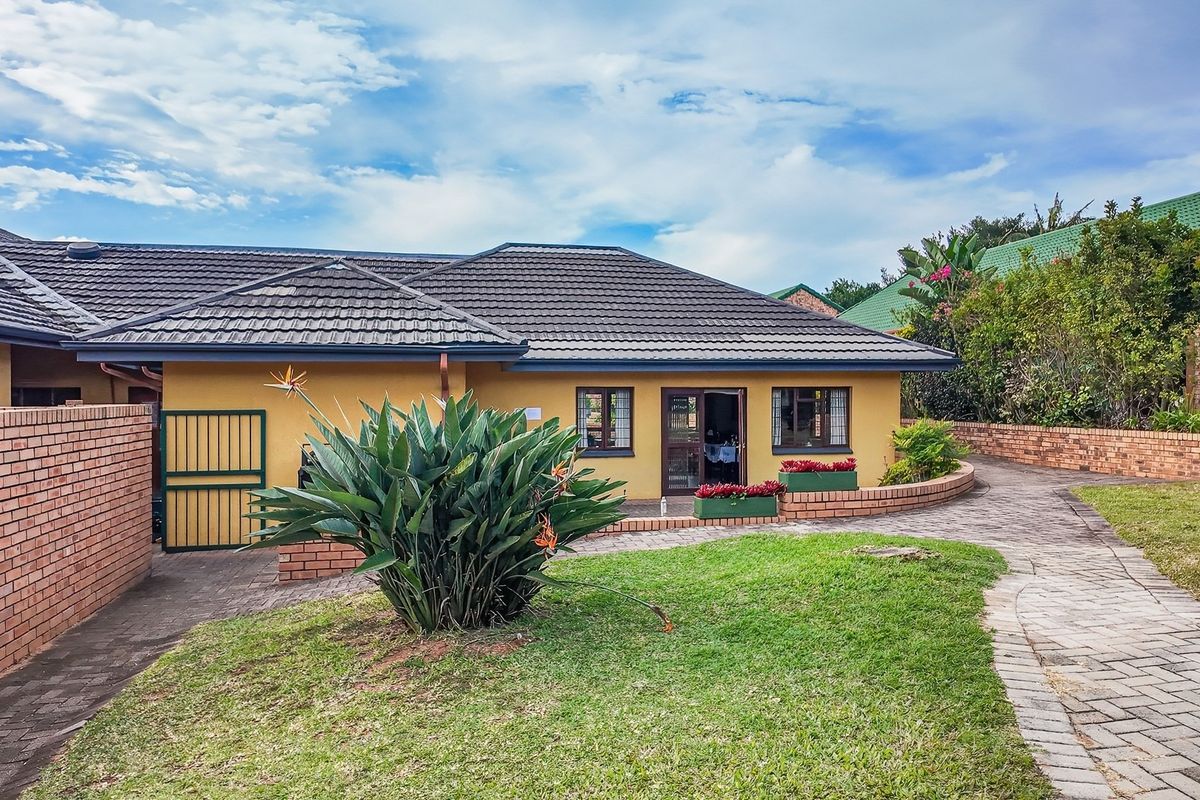 Rear view of a retirement village unit featuring a paved walkway, brick boundary walls, and a tiled roof with established garden surroundings.