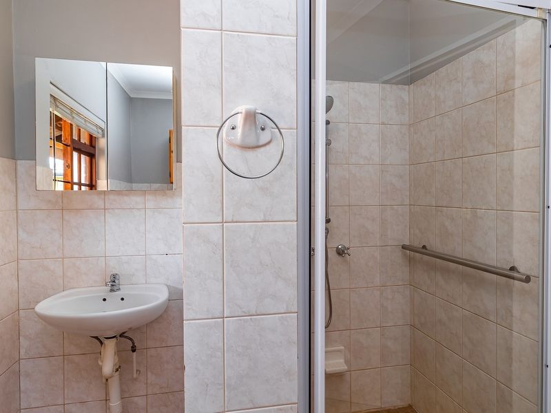 A functional bathroom featuring a wall-mounted basin, a tiled shower enclosure with a grab rail, and neutral wall tiling.
