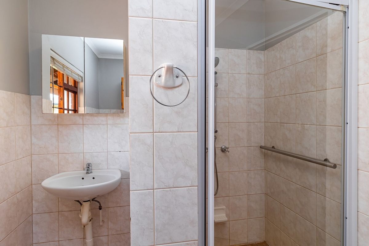 A functional bathroom featuring a wall-mounted basin, a tiled shower enclosure with a grab rail, and neutral wall tiling.