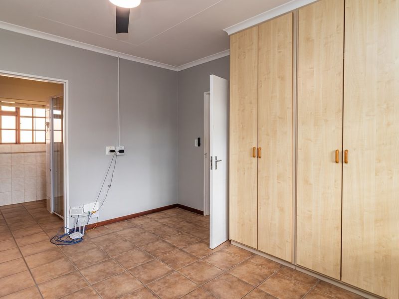 A spacious, empty bedroom featuring neutral grey walls, tiled flooring, and extensive built-in wooden cupboards, with direct access to an adjoining bathroom.