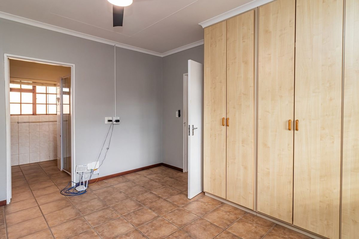 A spacious, empty bedroom featuring neutral grey walls, tiled flooring, and extensive built-in wooden cupboards, with direct access to an adjoining bathroom.