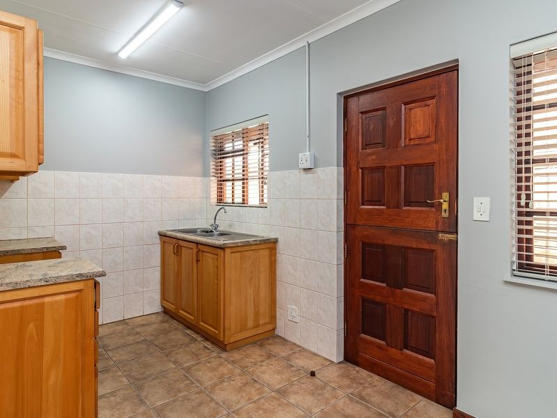 A functional scullery area featuring wooden cabinetry, a stainless steel sink, tiled splashbacks, and a classic wooden stable door leading to the exterior.
