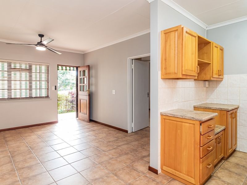Open-plan living area featuring tiled flooring, a ceiling fan, and a compact kitchen with wooden cabinetry and laminate countertops.