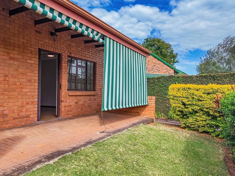 A well-maintained brick patio featuring a retractable striped awning, providing a comfortable outdoor space overlooking the private garden area.