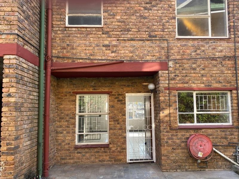 Rear exterior view of a face brick apartment building featuring a paved patio area, security gates, and a wall-mounted fire hose reel.