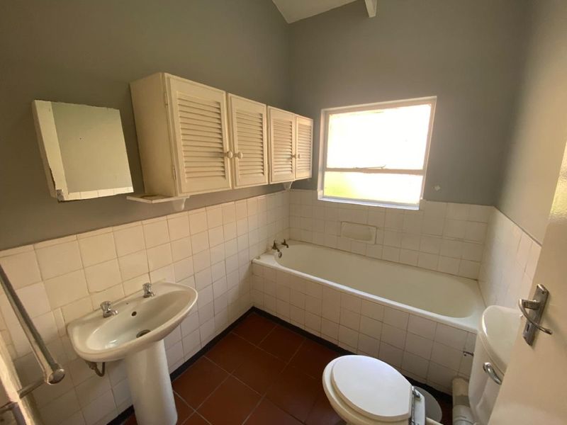 A dated bathroom featuring a pedestal basin, built-in wall cabinetry, and a tiled bathtub with ceramic wall and floor finishes.
