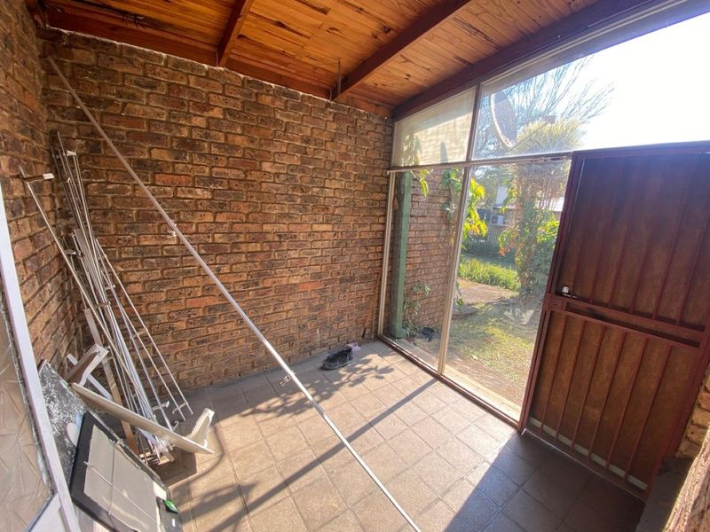 A covered patio area featuring exposed timber ceilings, facebrick walls, and tiled flooring, providing direct access to the garden through a large glass sliding door.