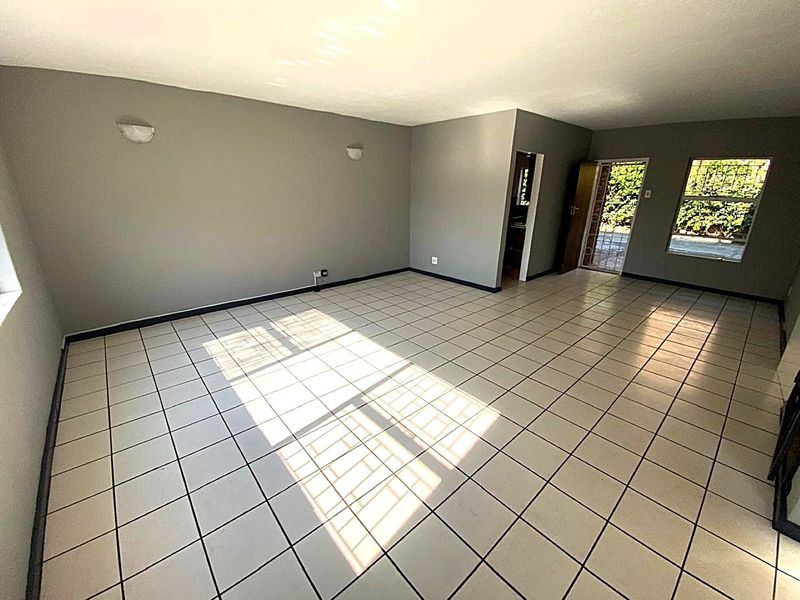 A spacious, empty living area featuring neutral grey walls, ceramic tiled flooring, and natural light entering through windows with security bars.