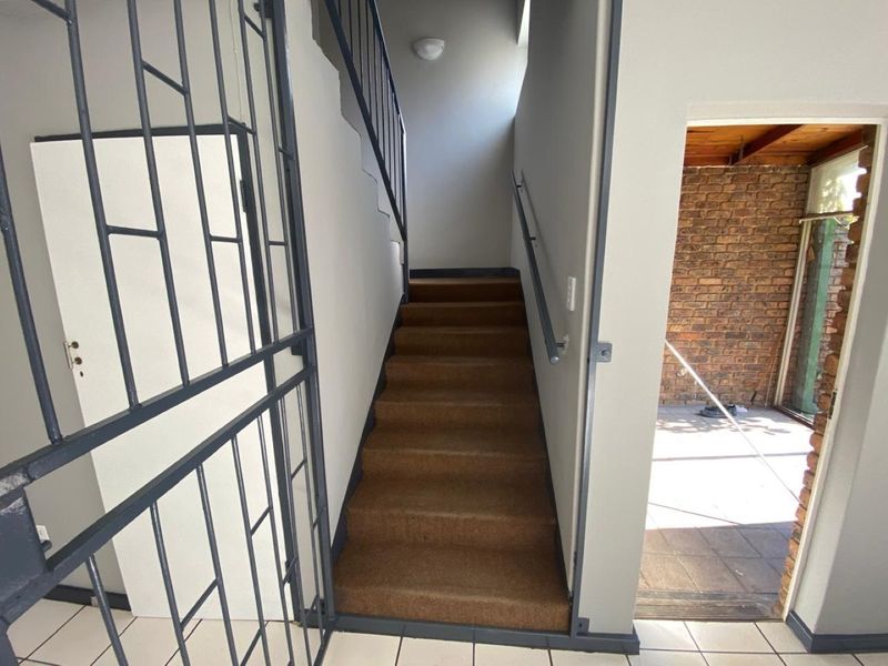 An interior entry area featuring a staircase with a handrail, a security gate, and tiled flooring, leading towards an outdoor patio space.
