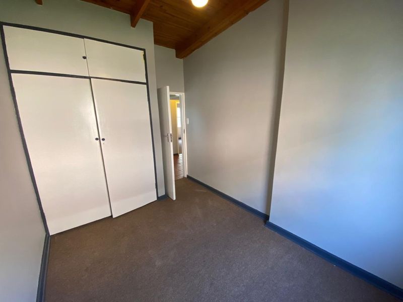 A vacant bedroom featuring built-in cupboards, exposed timber ceiling beams, and carpeted flooring.