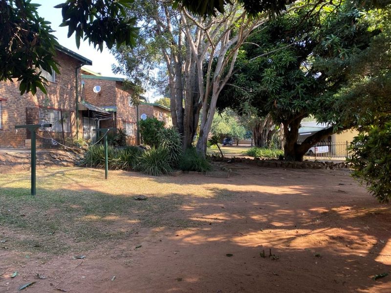 A view of the rear exterior area featuring a face brick apartment building facade, mature trees, and a large open garden space.
