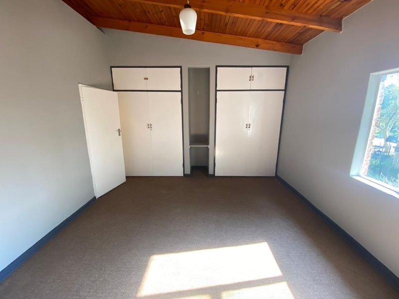 An empty bedroom featuring built-in cupboards, carpeted flooring, and an exposed timber ceiling with a pendant light fixture.