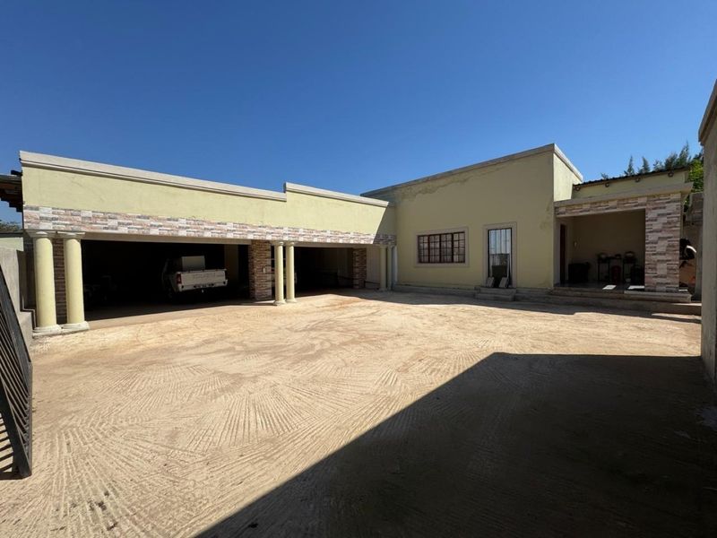 Exterior view of a farm property featuring a large sand driveway, covered parking area with columns, and stone-clad accents on the building facade.