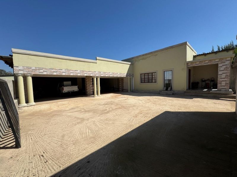 Front exterior view of a farm property featuring a triple garage with stone cladding, concrete columns, and a large unpaved driveway area.