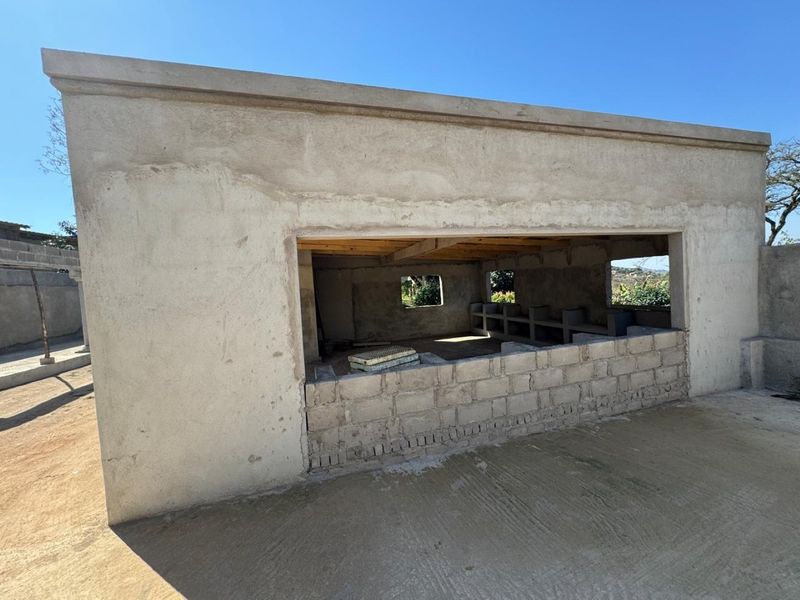 An unfinished outdoor structure featuring exposed concrete block walls, a cement floor, and an open-plan design, currently in the early stages of construction.