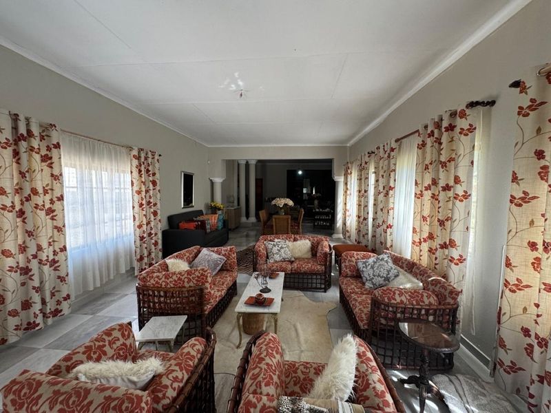 Spacious open-plan living and dining area featuring tiled flooring, decorative columns, and large windows with natural light.