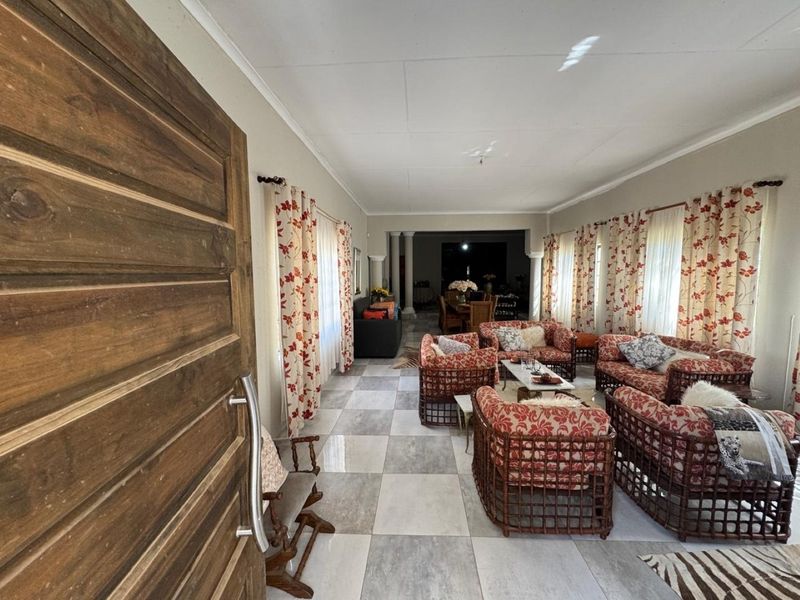 Spacious living area featuring large format floor tiles, a solid wooden entrance door, and architectural columns leading to an adjacent dining space.