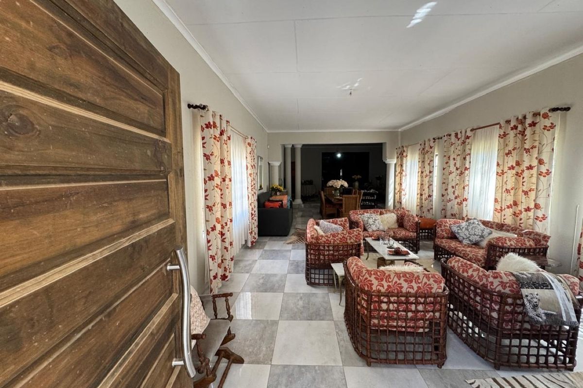 Spacious living area featuring large format floor tiles, a solid wooden entrance door, and architectural columns leading to an adjacent dining space.