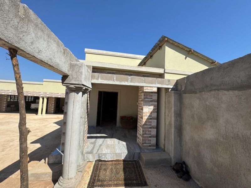 Front entrance area of a farm property featuring stone columns, tiled porch flooring, and unfinished concrete boundary walls.