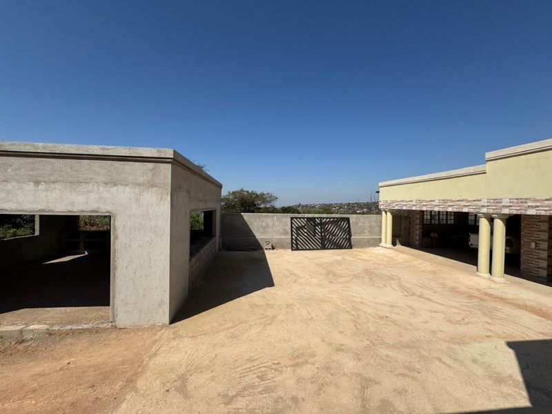An expansive outdoor courtyard area featuring unfinished concrete structures, stone-clad pillars, and a metal gate, offering potential for landscaping and development.