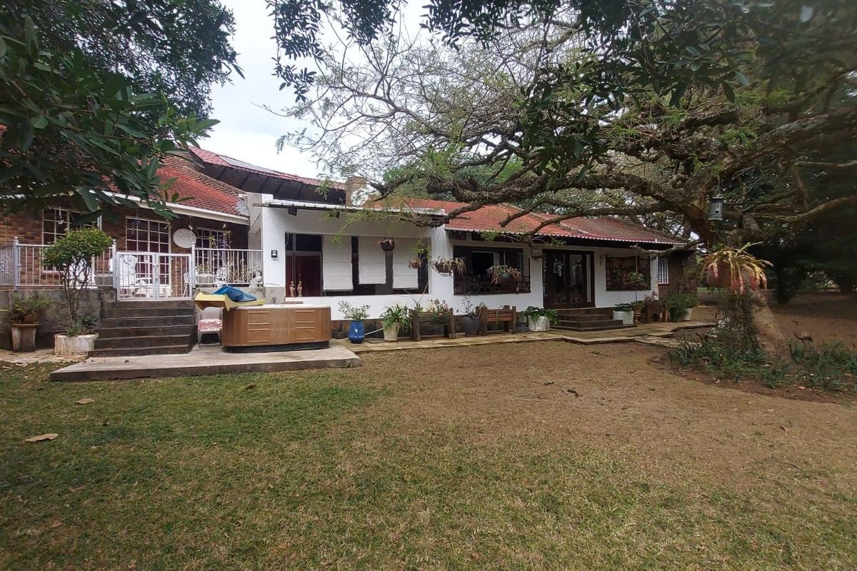 Rear view of the small holding residence featuring a tiled roof, brick and plaster facade, and a concrete patio area overlooking the garden.