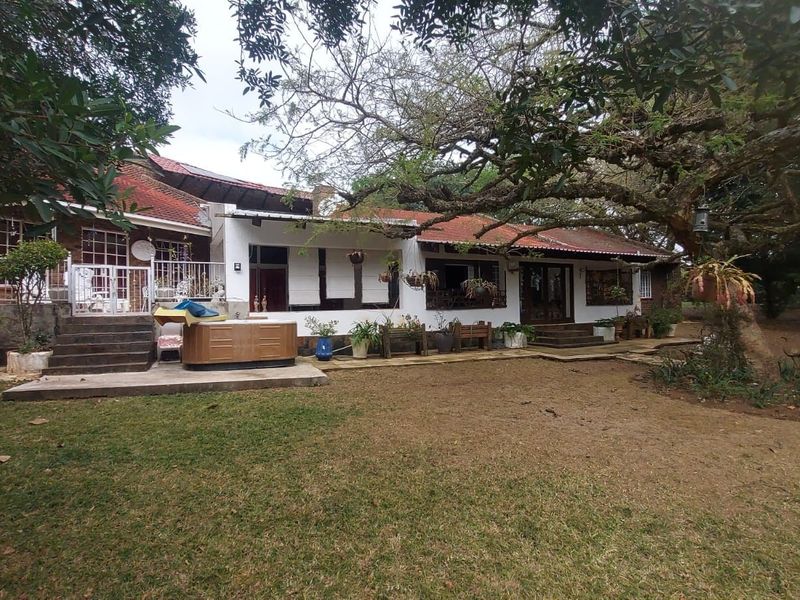 Rear view of the small holding residence featuring a tiled roof, brick and plaster facade, and a concrete patio area overlooking the garden.