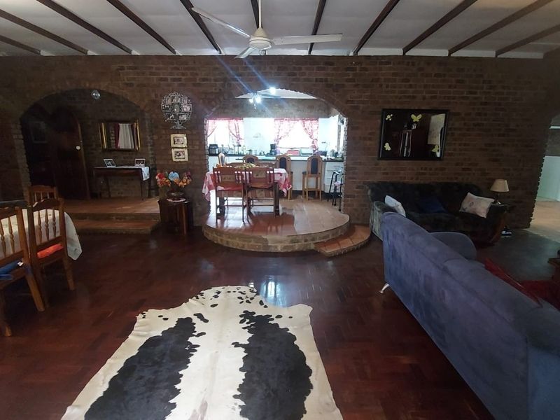 Spacious open-plan living and dining area featuring rustic exposed brick walls, timber beam ceilings, and parquet flooring with a raised dining platform.