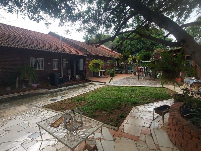 Rear exterior view of a brick-built small holding featuring a paved patio area, central lawn, and established garden surroundings.
