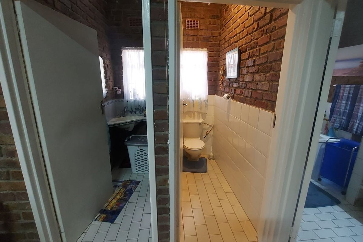 A functional bathroom featuring exposed brick walls, tiled flooring, and a standard pedestal basin and toilet setup, requiring cosmetic updates.