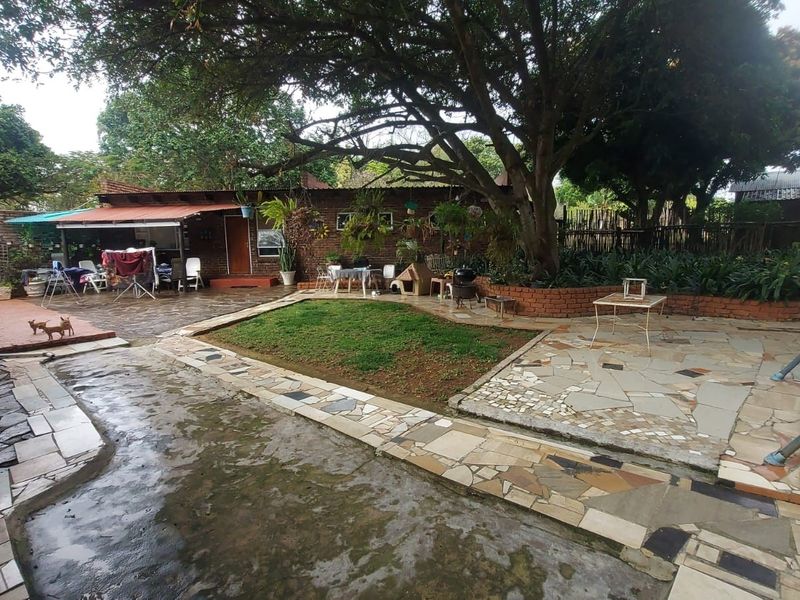 A rear garden area featuring a covered patio, brick and stone paving, and a large mature tree providing shade over the outdoor space.