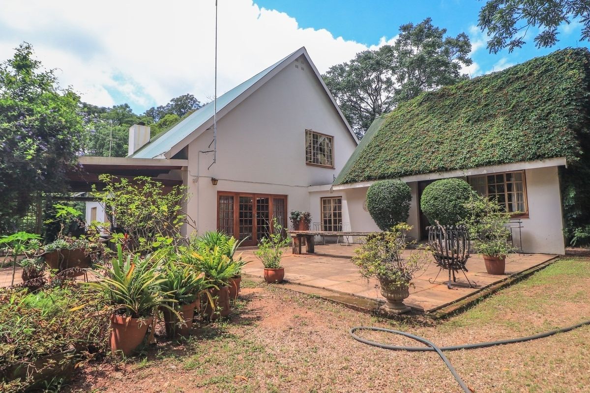 Rear view of the property featuring a paved patio area, timber-framed doors, and a distinctive thatched roof section.