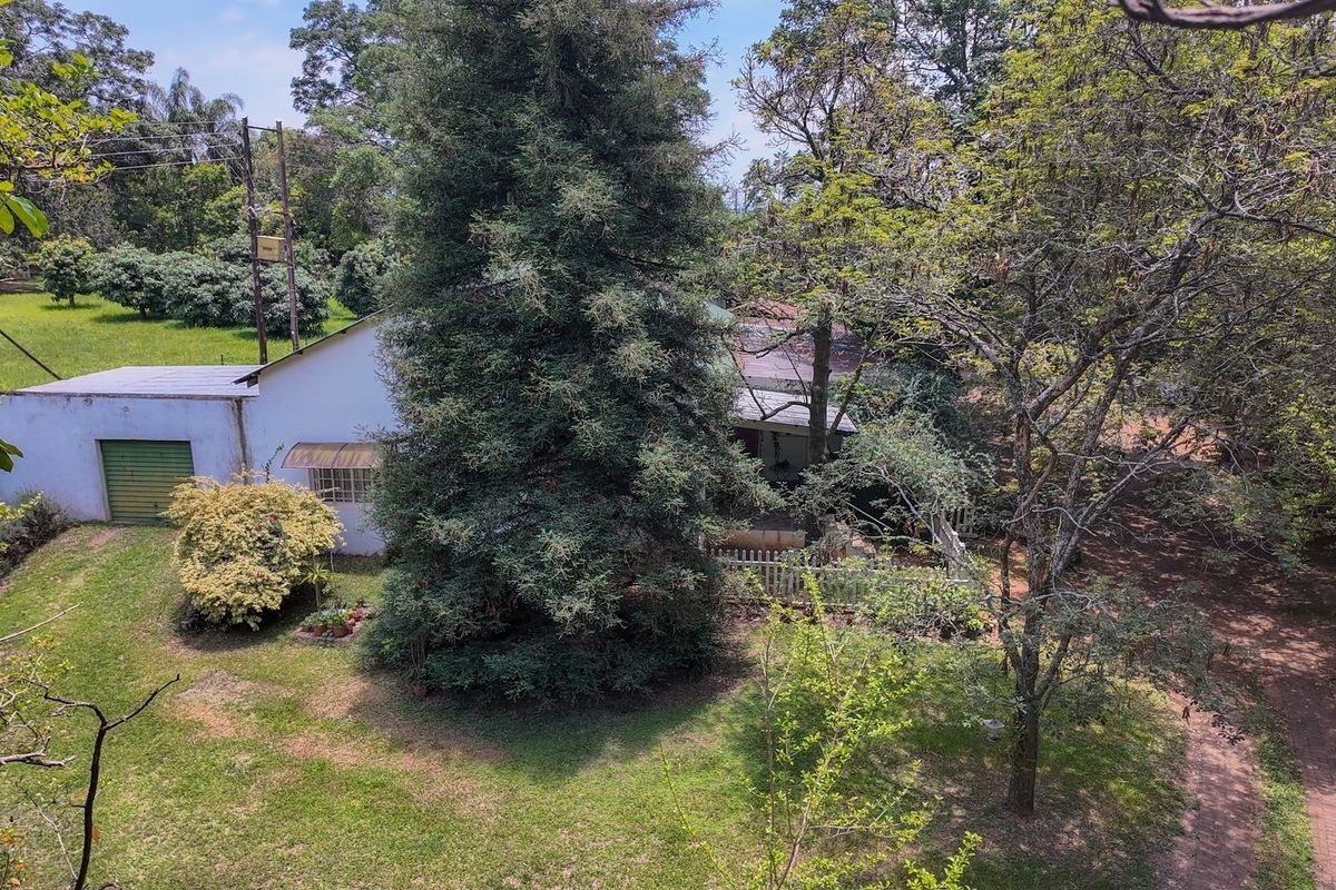 An elevated aerial view of the property grounds, featuring a garage, expansive lawn, mature trees, and a paved driveway on a small holding.