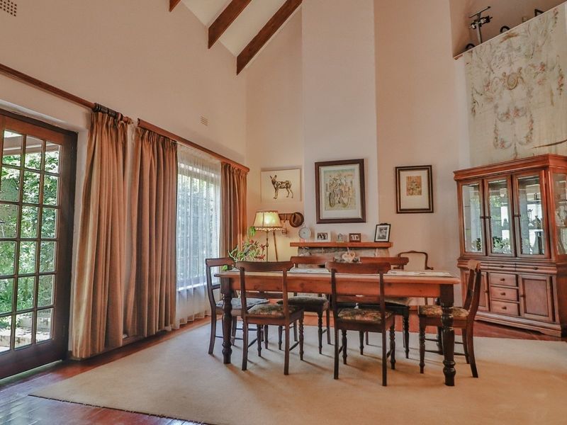 Spacious dining room featuring vaulted ceilings with exposed timber beams, a traditional fireplace, and direct access to the garden through classic french doors.