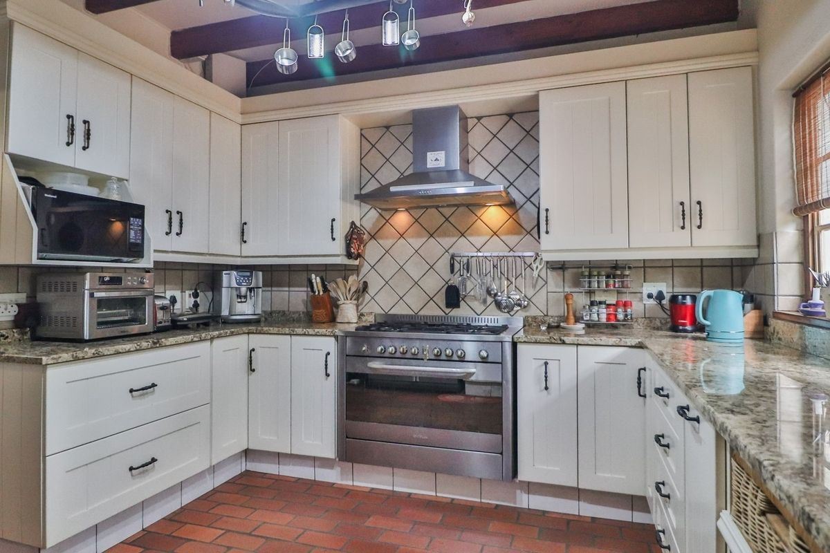 A well-appointed kitchen featuring granite countertops, a stainless steel gas stove with extractor, and classic cabinetry with exposed timber ceiling beams.
