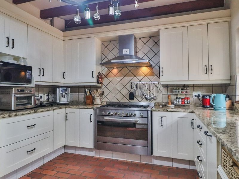 A well-appointed kitchen featuring granite countertops, a stainless steel gas stove with extractor, and classic cabinetry with exposed timber ceiling beams.