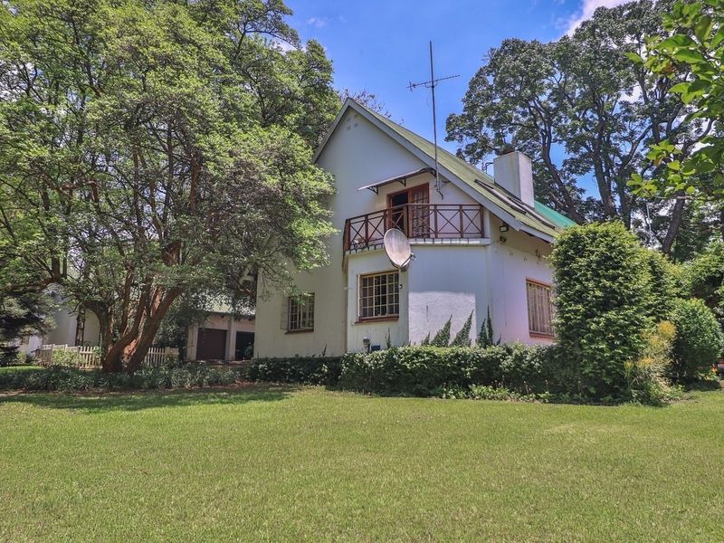 Rear view of a double-story residence featuring a balcony, mature garden surroundings, and established trees on a spacious small holding property.