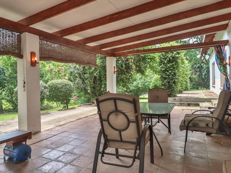 A spacious covered patio featuring exposed timber beams, tiled flooring, and direct access to the lush garden, ideal for outdoor entertaining.