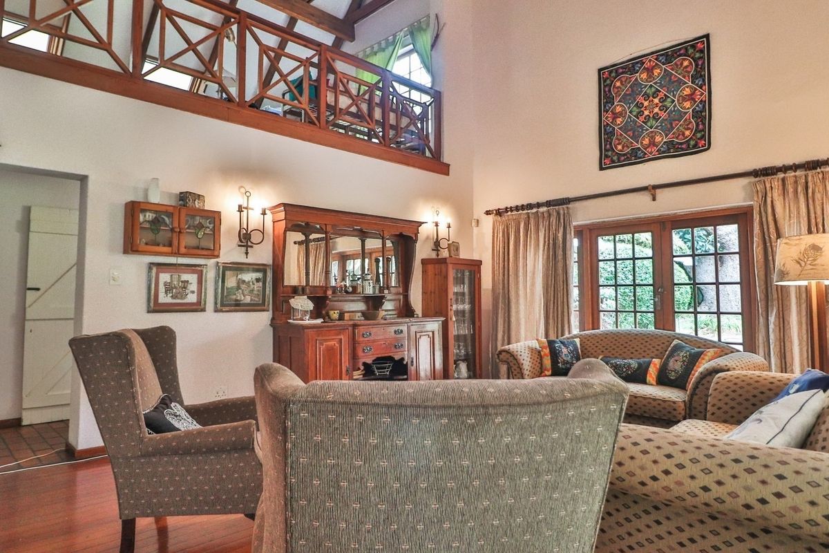 Spacious double-volume living room featuring exposed timber beams, a mezzanine level with wooden balustrade, hardwood flooring, and direct access to the garden via french doors.