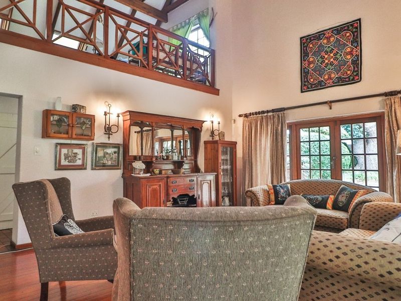 Spacious double-volume living room featuring exposed timber beams, a mezzanine level with wooden balustrade, hardwood flooring, and direct access to the garden via french doors.