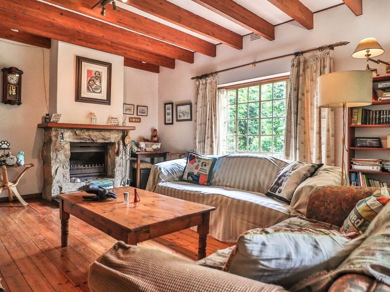 Cozy living room featuring exposed timber ceiling beams, a rustic stone fireplace, and warm timber flooring, creating a comfortable and inviting atmosphere.