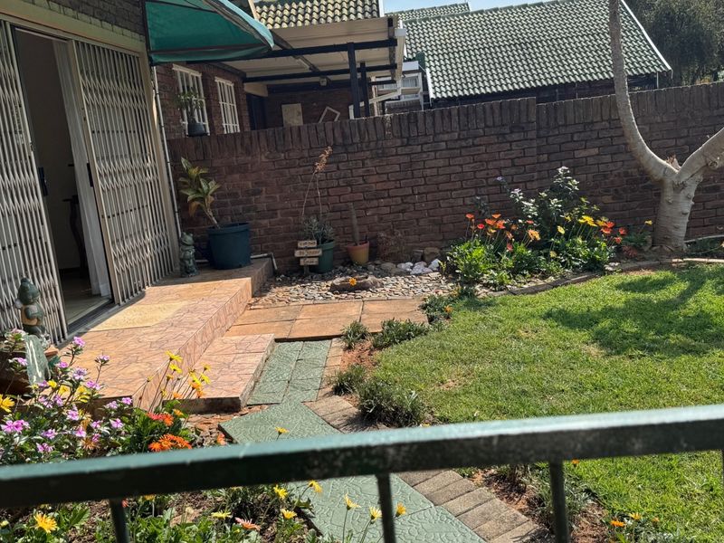 A private rear garden featuring a tiled patio area, brick boundary wall, paved pathway, and established lawn.